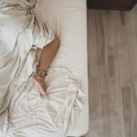 Modernaus dizaino intymios gerovės prietaisas ant naktinio stalelio šalia degančios žvakės ir knygos.